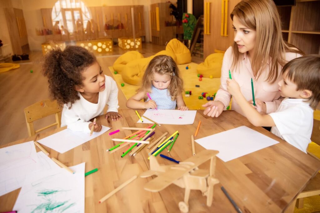 Educator speaking to children while they draw at a daycare center in Red Oak, TX.